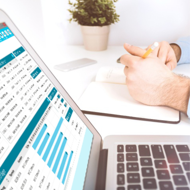 Nahaufnahme Laptop auf Tisch zeigt die neue Oberfläche, im Hintergrund sind Hände zu sehen, die mit einem Stift in ein Notizbuch schreiben.