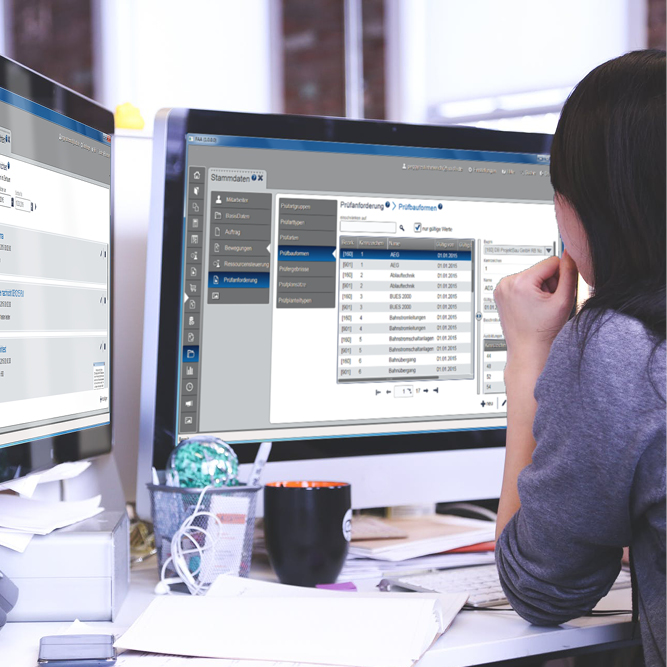 Person an Arbeitsplatz vor zwei Monitoren, die die neue Oberfläche zur Verwaltung von Personenverkehr zeigen, der Person wird über die Schulter geschaut.